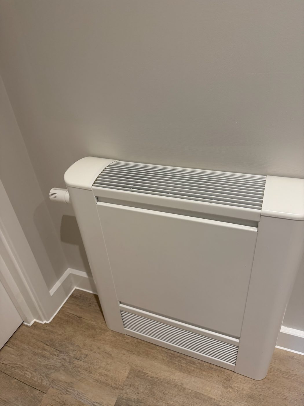 Low level indoor fan convector unit fitted against a wall in a finished room