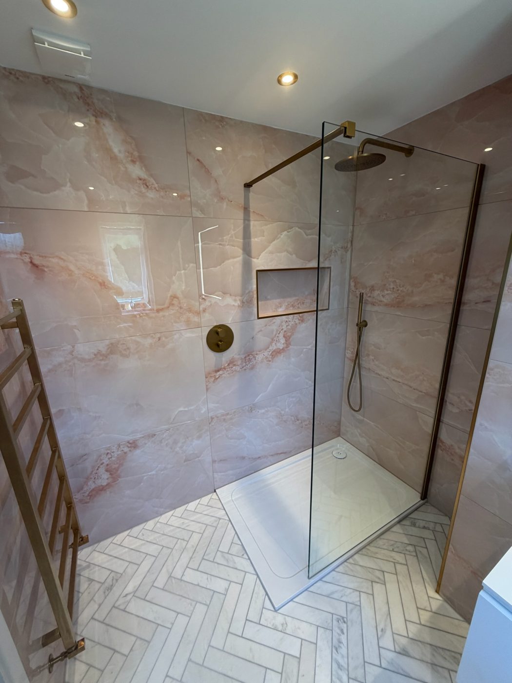 Walk in shower with marble effect tiling, brass fittings and herringbone floor