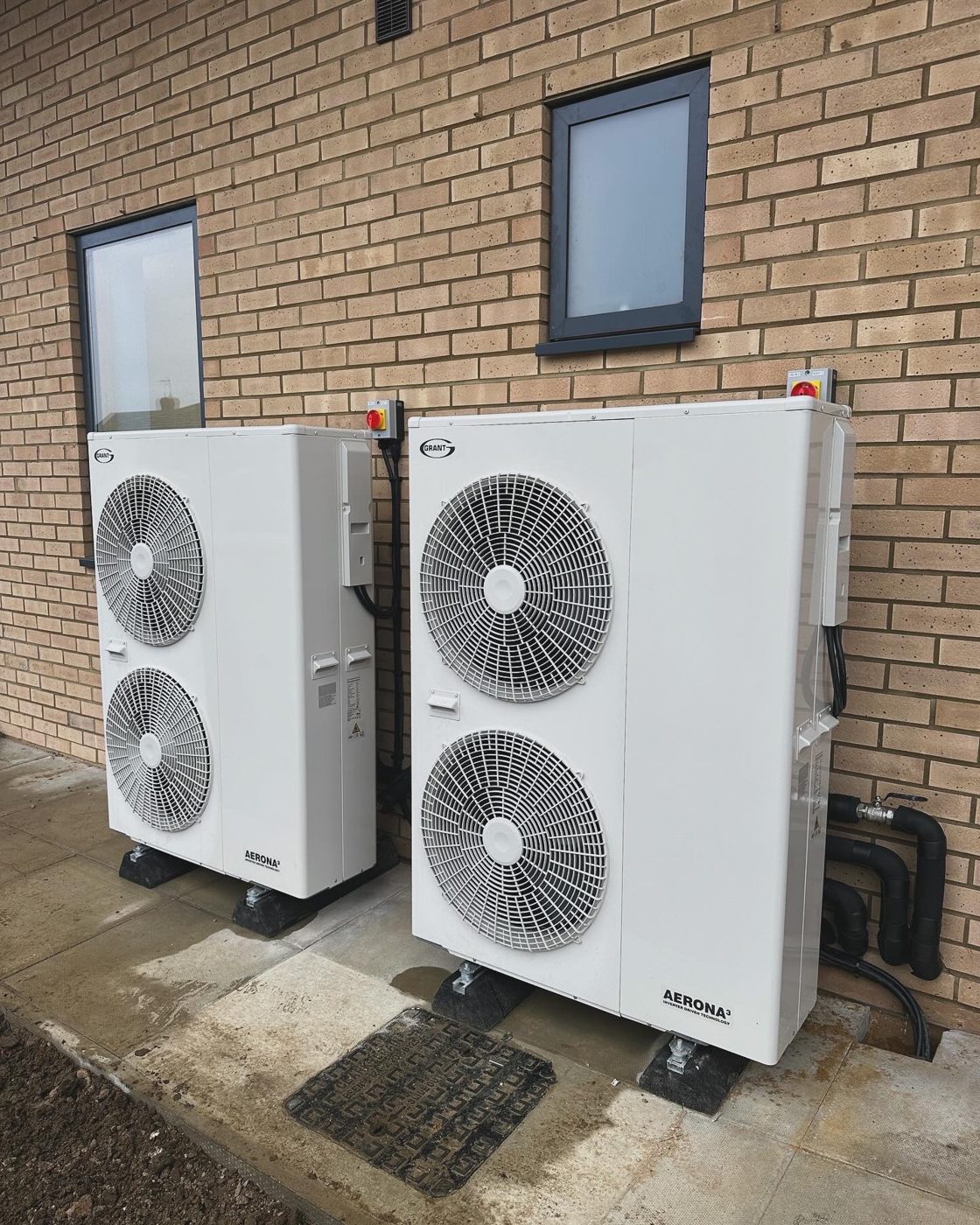 Two outdoor heating and cooling units mounted against a brick wall