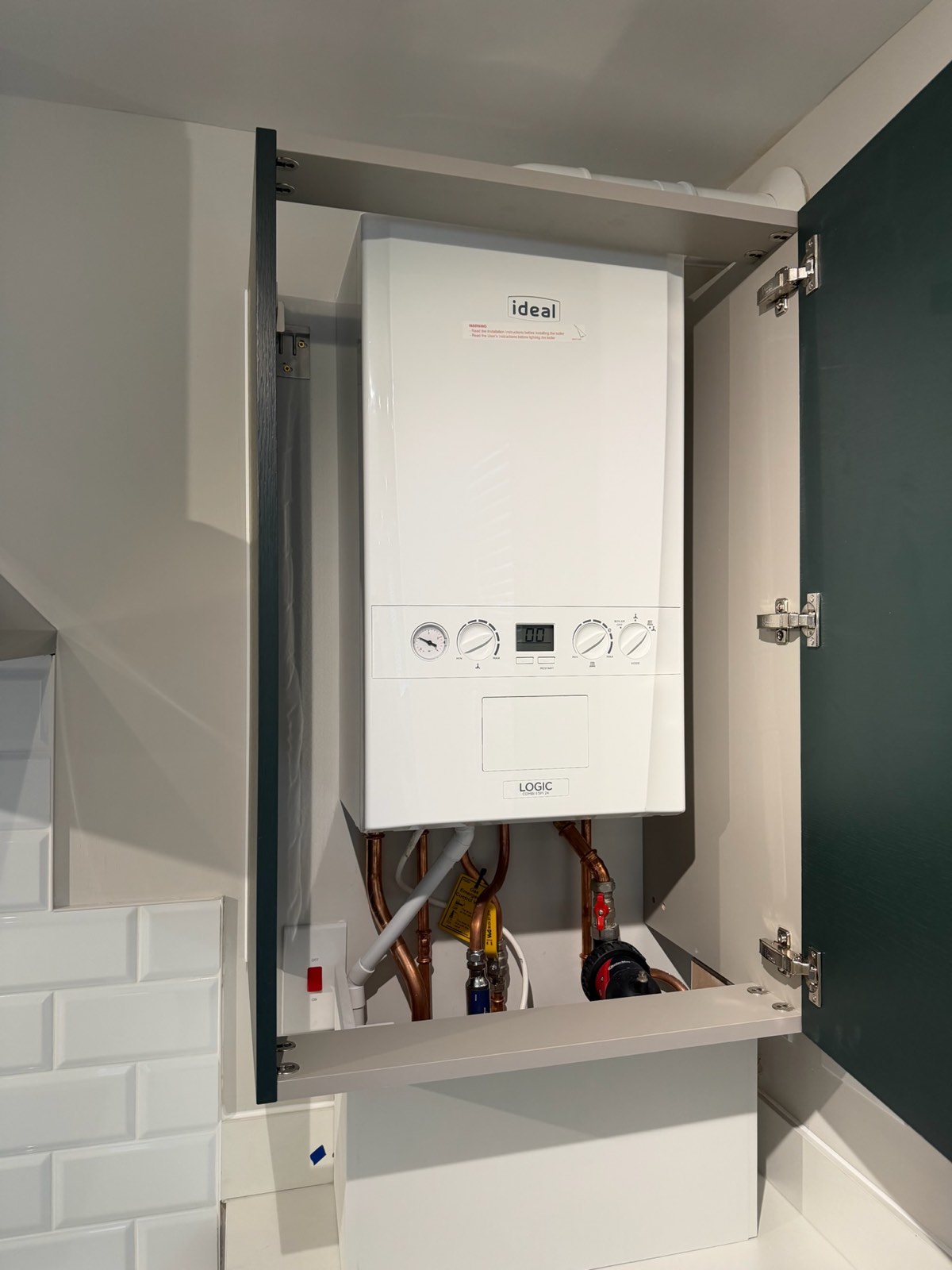 Concealed combi boiler installation inside a fitted green kitchen cupboard