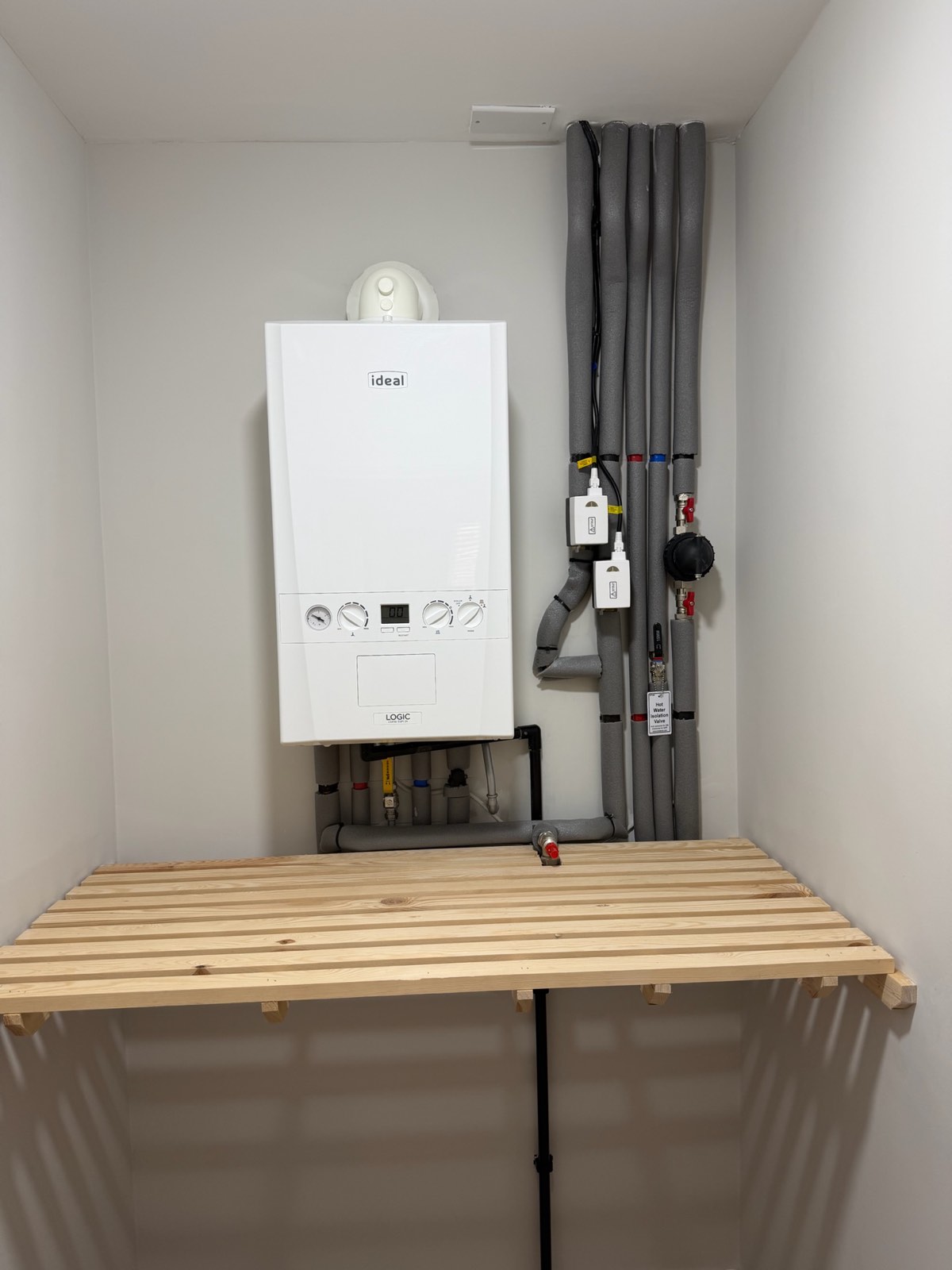 Airing-cupboard boiler with insulated hot and cold risers and labelled isolation valves