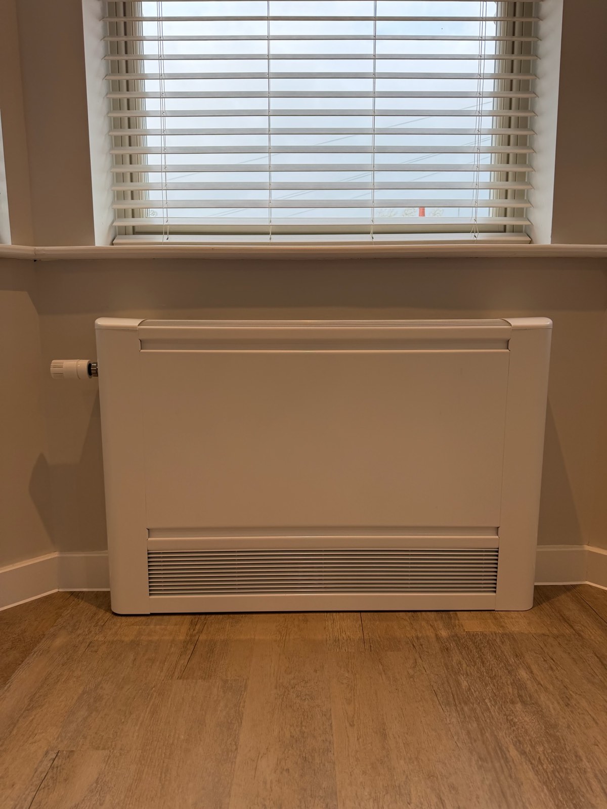 Wall-mounted low-surface-temperature radiator beneath a window in a finished apartment