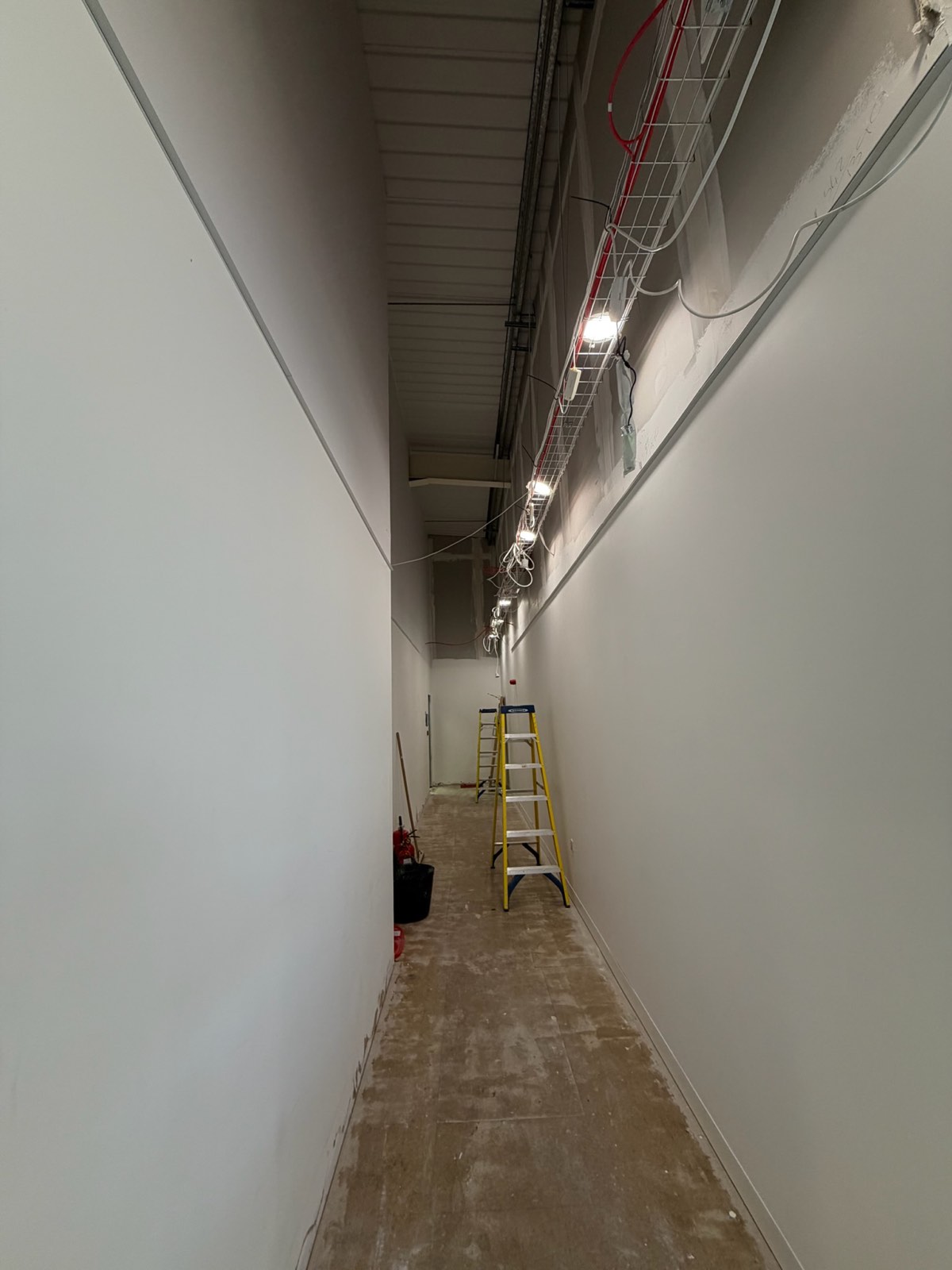Long corridor first-fix with cable tray, fire main and temporary site lighting