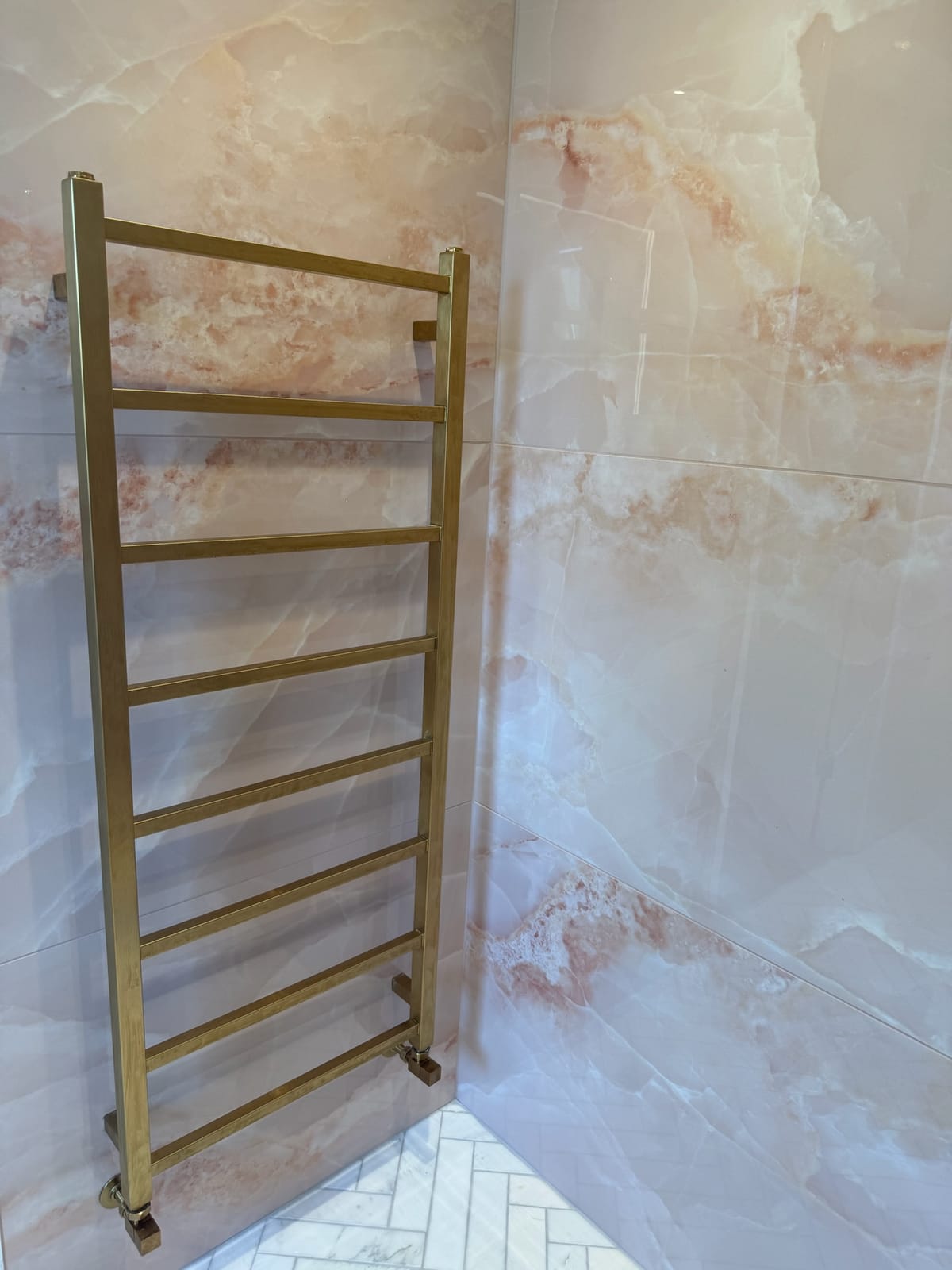 Brushed brass heated towel rail against onyx-effect wall tiling