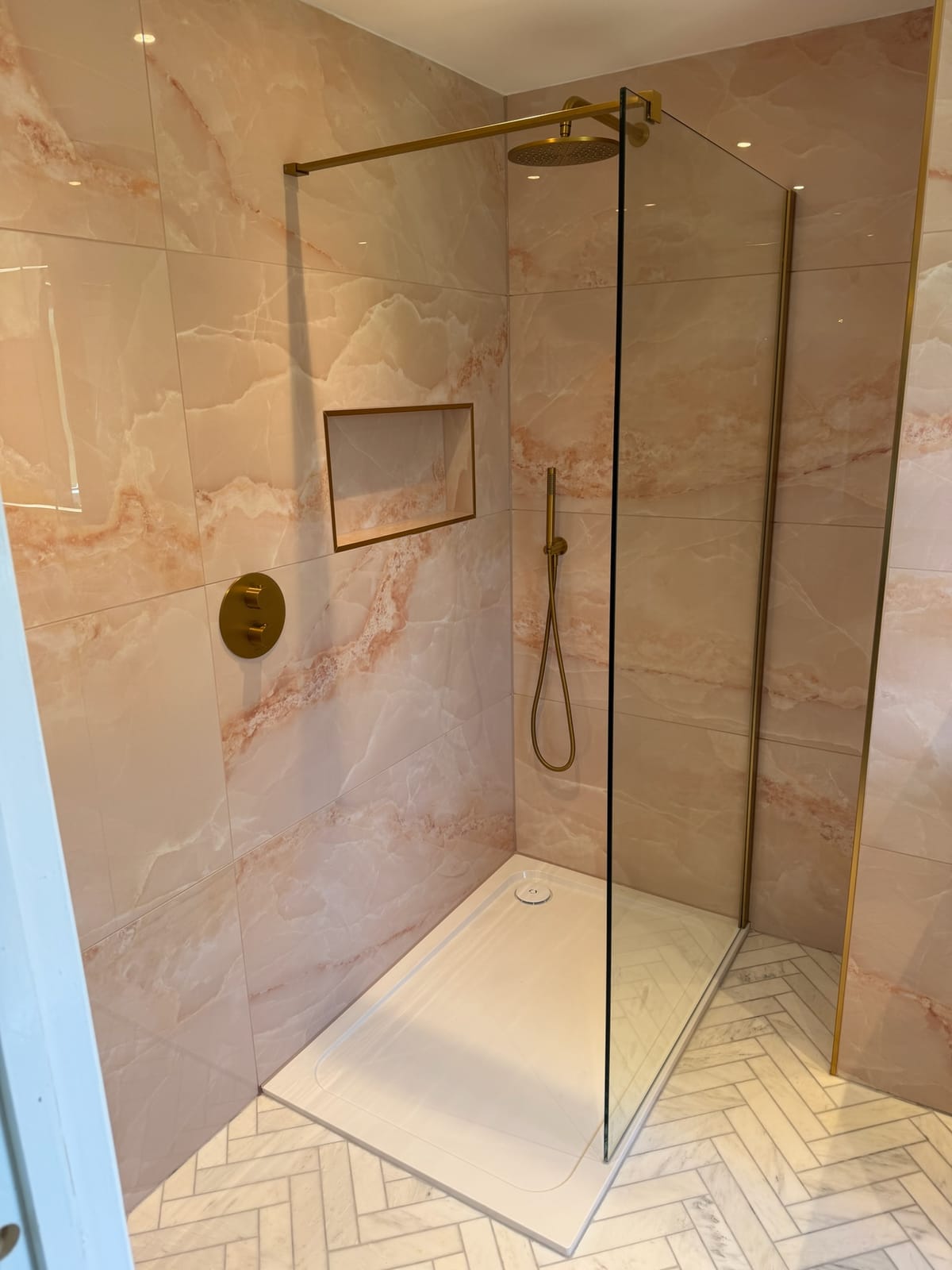Walk-in shower with onyx-effect porcelain tiling, brushed brass fittings and a marble herringbone floor