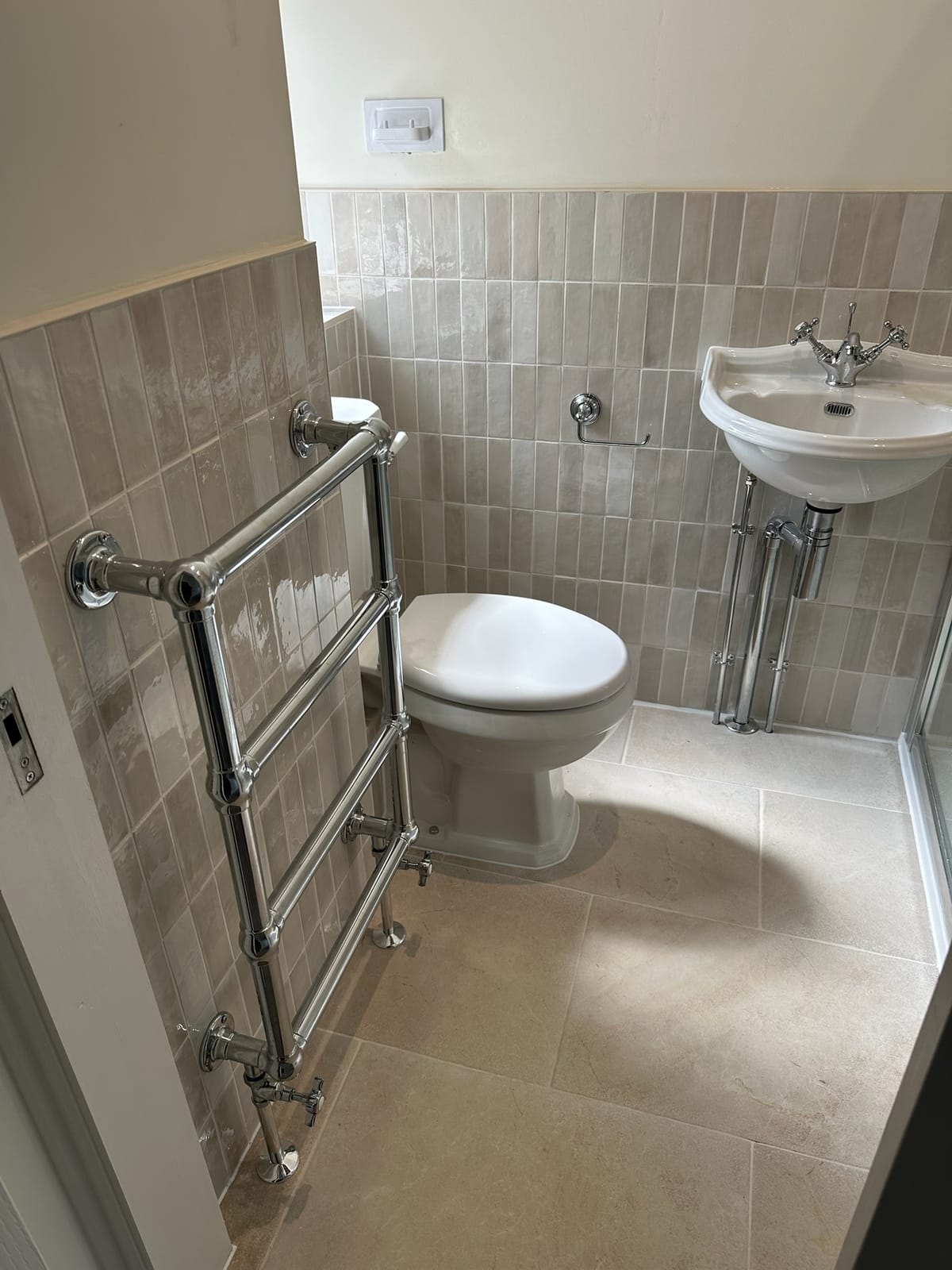 Traditional cloakroom with chrome heated towel rail, corner basin and metro tiling
